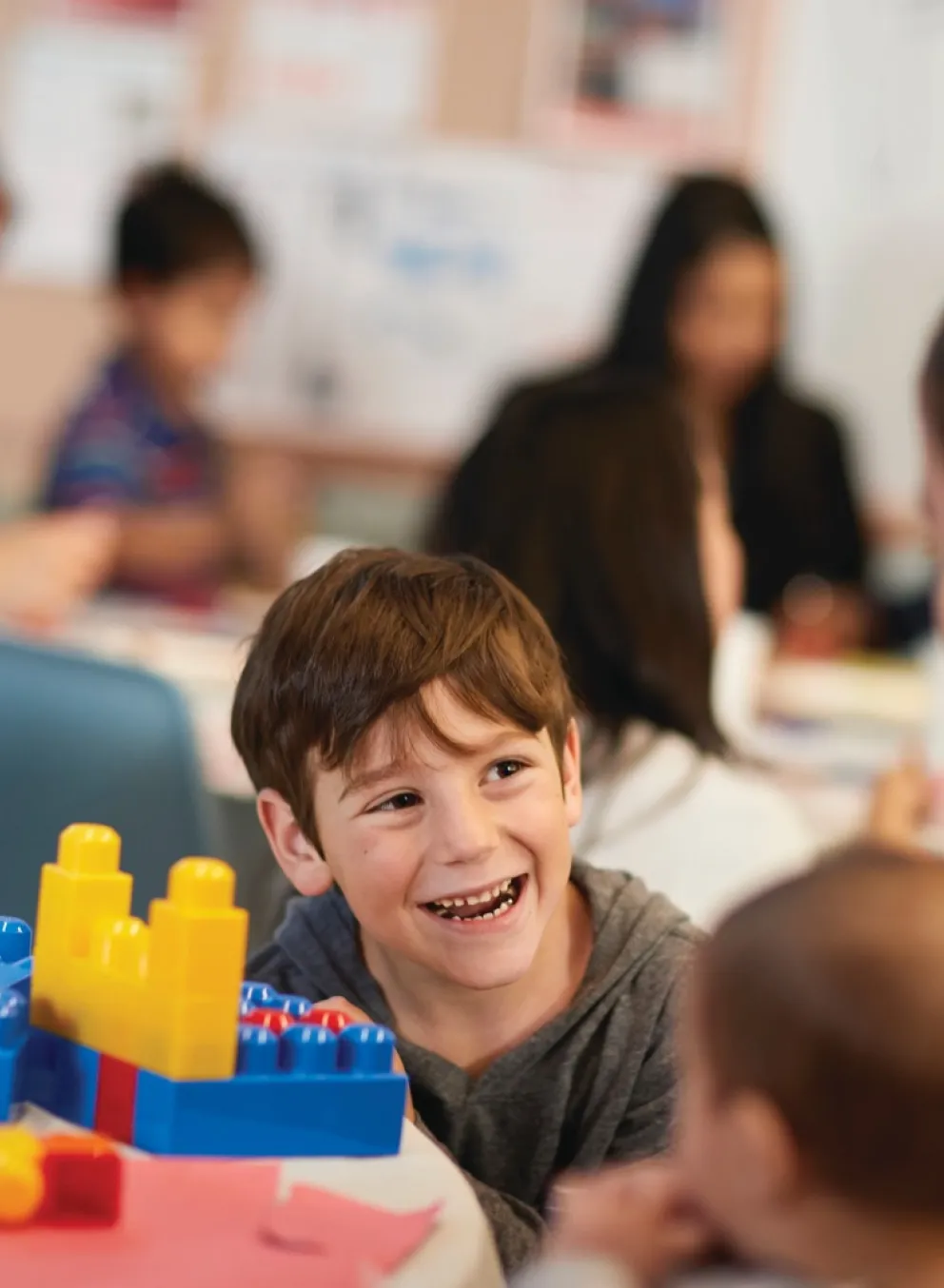 A child smiles while building with colorful blocks alongside an adult.