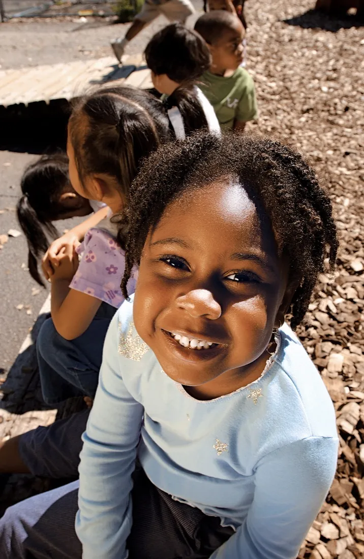 A smiling child enjoys time outdoors with other children.
